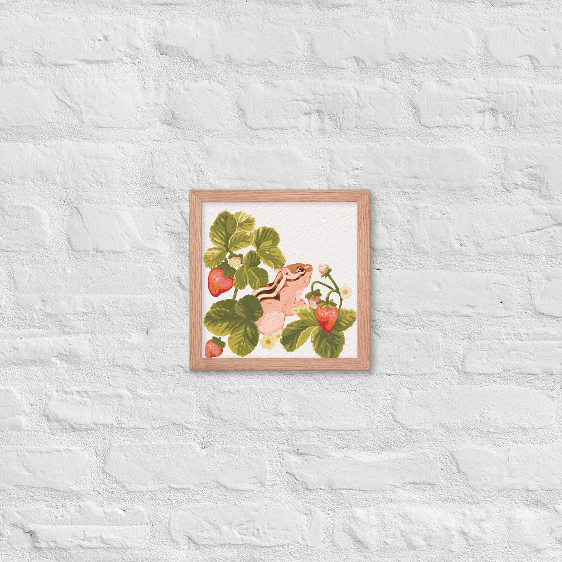 Framed artwork of a chipmunk among strawberry plants on a textured white wall.